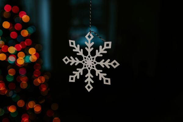 Gold metal snowflake hanging from string with colors in backgrond.