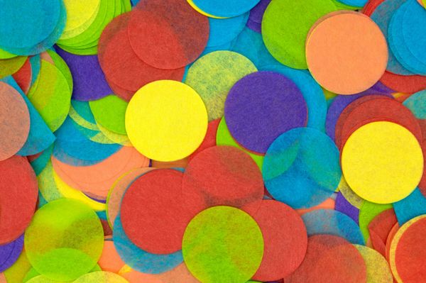 Brightly colored round confetti pieces in shades of yellow, red, blue, green, orange, and purple overlapping in a festive, te