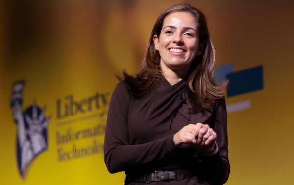 Monica Caldas, global CIO at Liberty Mutual Insurance Company smiling in front of the Liberty Mutual logo.