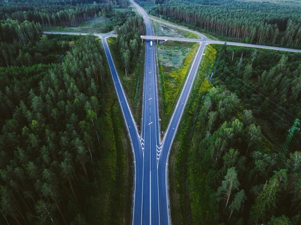 Aerial view of a highway splitting into two directions through a dense green forest, symbolizing a crossroads or decision poi