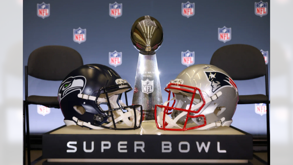 The Vince Lombardi Trophy positioned between football helmets from the Seattle Seahawks and New England Patriots at a Super Bowl event.