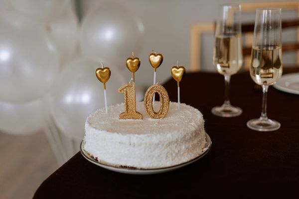 White cake with gold “10” candles, champagne glasses, balloons behind.