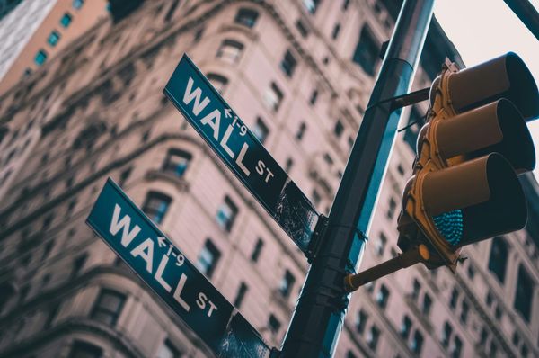 Two Wall St street signs on a light pole from ground up view.