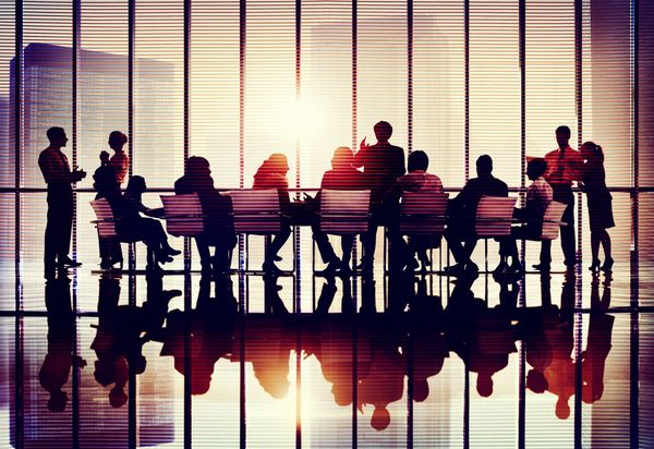 Silhouettes of business people meeting in a glass-walled office at sunset.