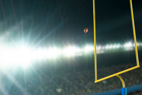 A football sailing through yellow goalposts under bright stadium lights
