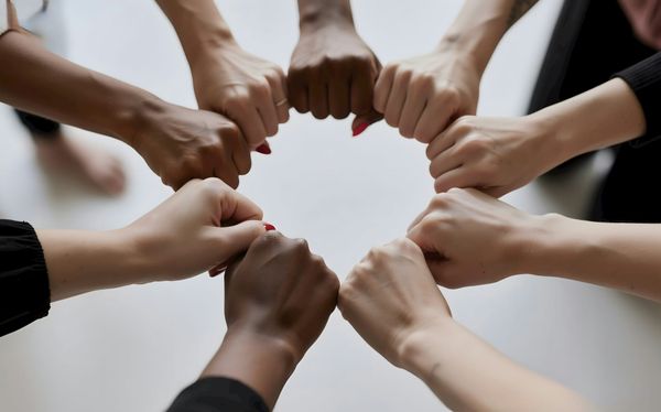 Several hands form a circle of fist bumps, shot from below.