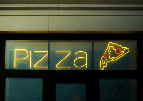 Neon Pizza sign with glowing slice of pepperoni pizza displayed in a storefront window at night.
