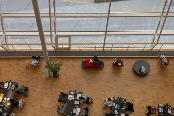 People work, read and use laptops in a bright, open atrium viewed from above.
