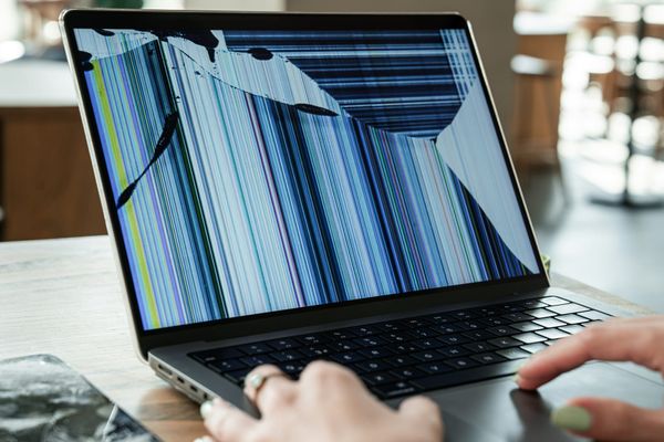 Laptop with a cracked screen displaying distorted vertical lines.