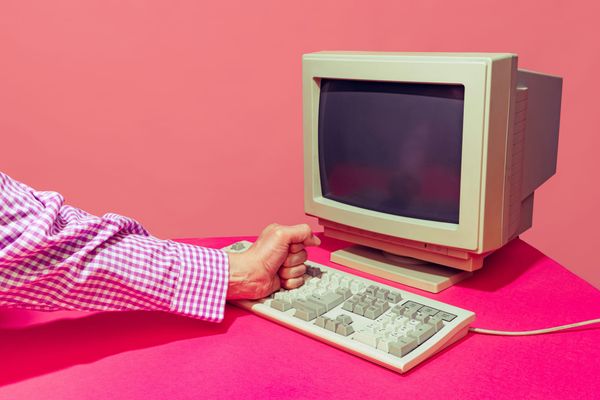 Person pounding a fist beside a vintage computer and keyboard.