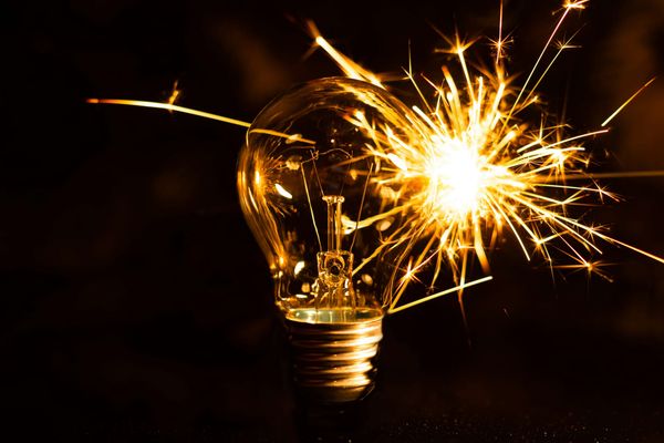 Glowing light bulb surrounded by bright sparks against a dark background.