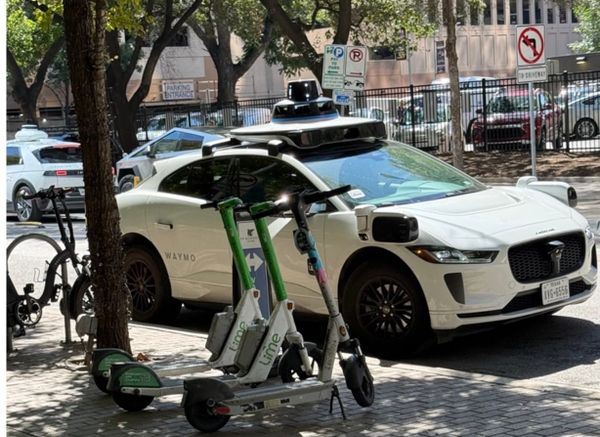 Waymo self-driving vehicle with lime scooters on street in Austin, Texas.