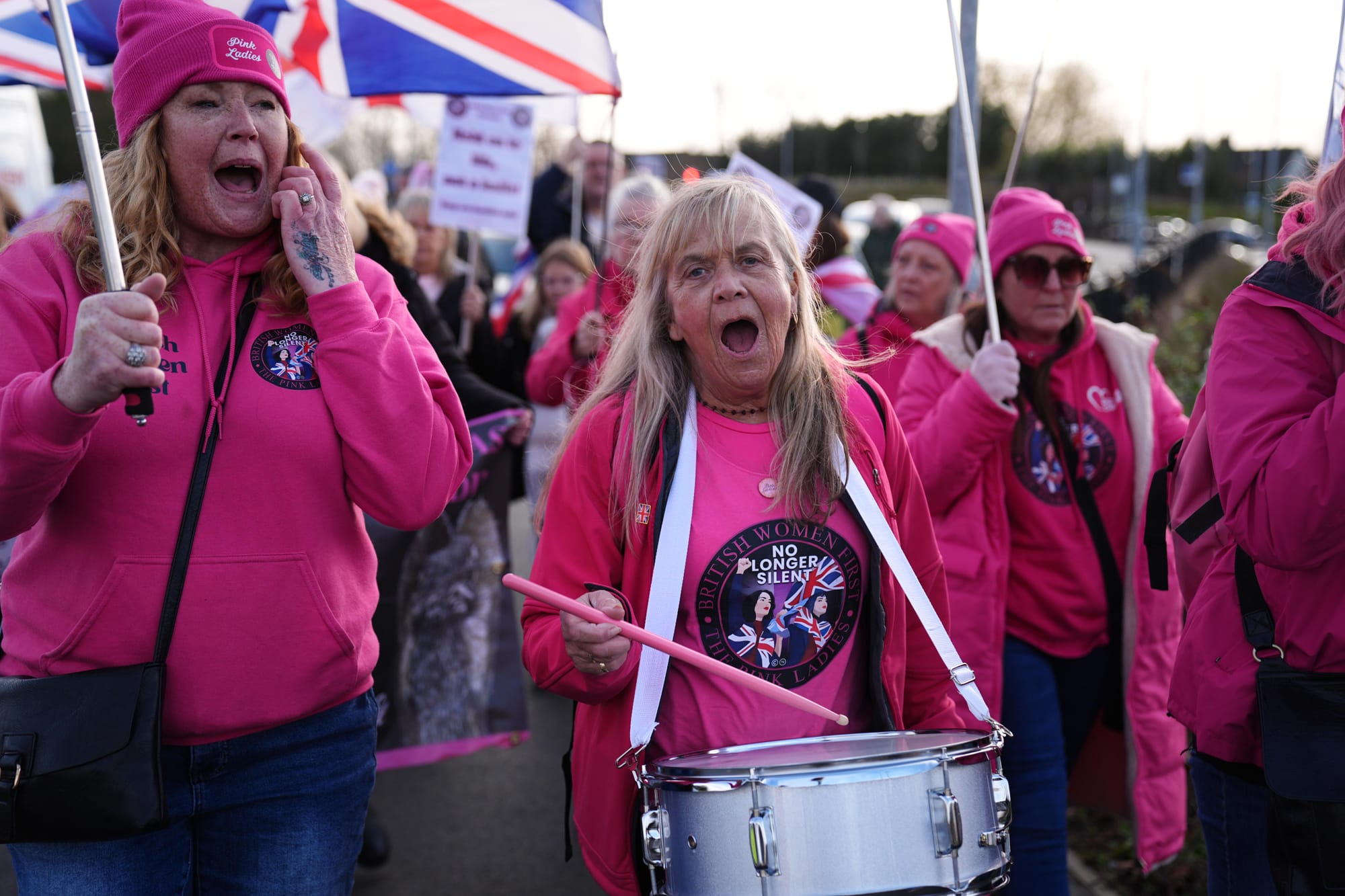Women at a protest dressed in hot pink, one banging a drum around her neck