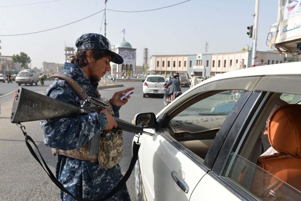 A photo of a Taliban soldier pointing a weapon at a driver at a checkpoint