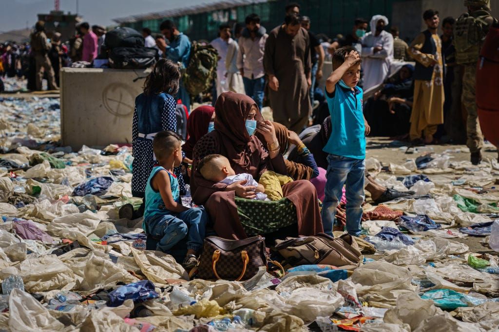 A photo of an Afghan woman holding a child as she sits with other children on a pile of trash and debris