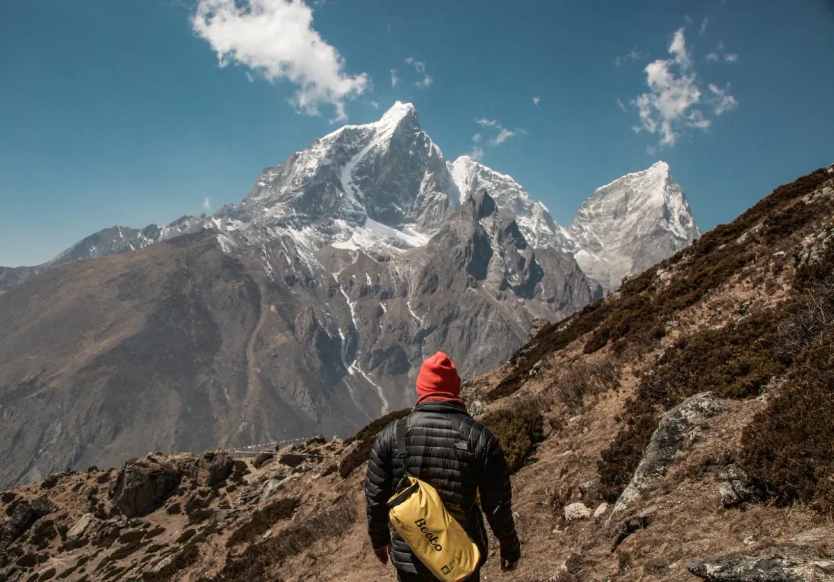 Hiker with a backpack facing a vast snow-capped mountain, the long climb of a software career