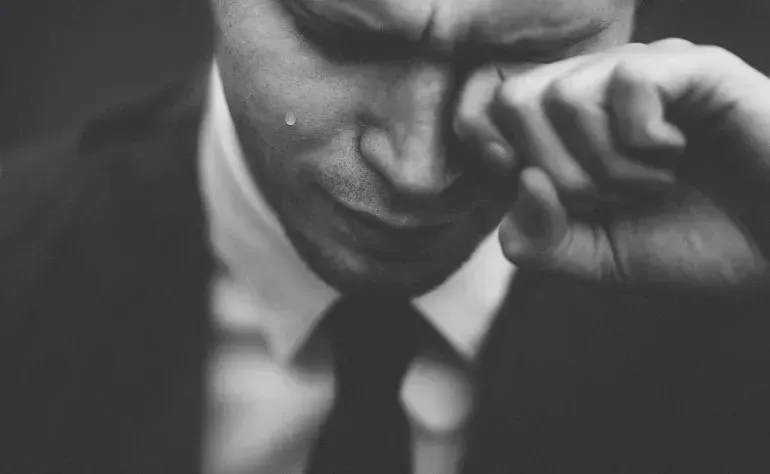 A man in a suit wiping away a tear, evoking the human cost of toxic team management.