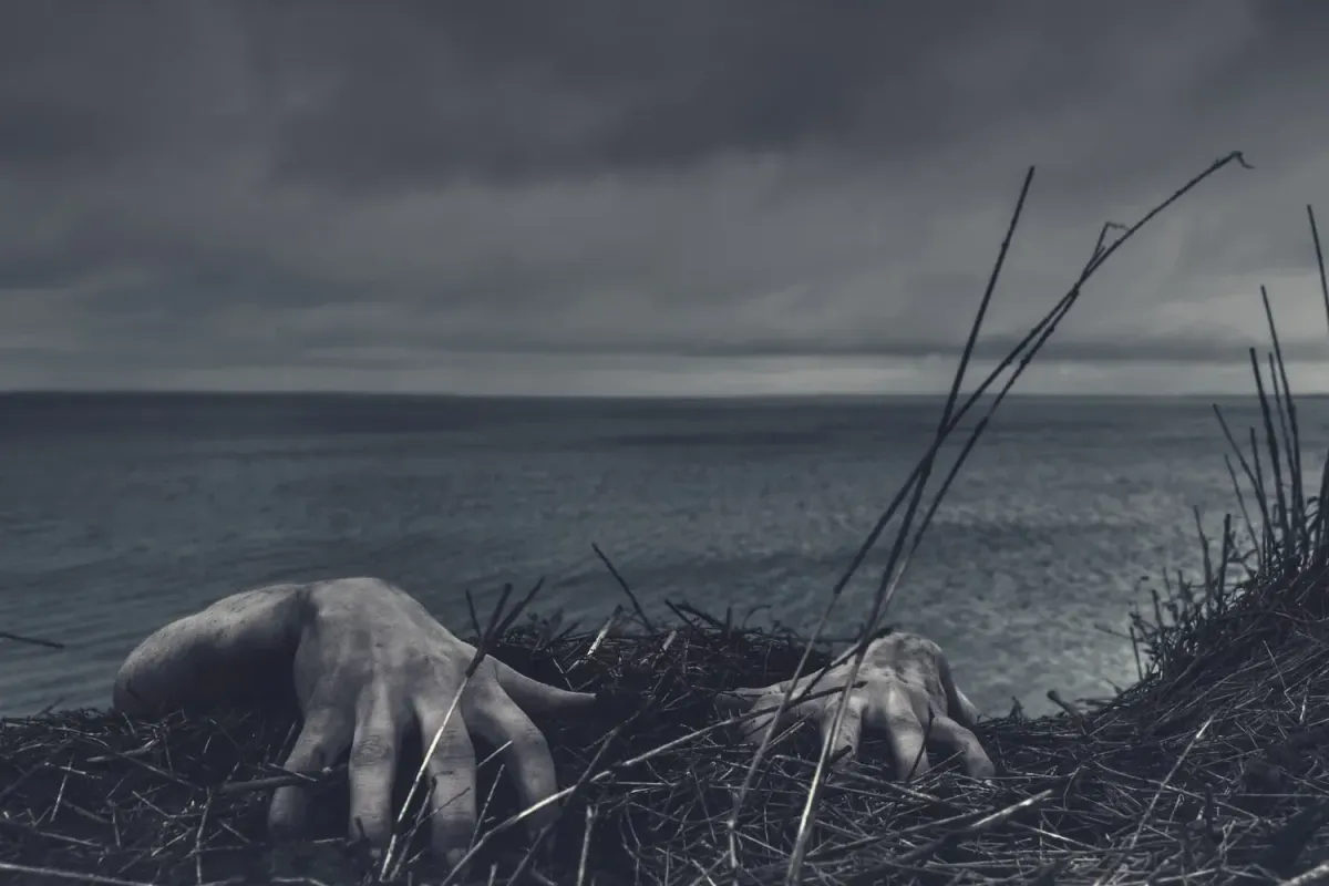 Two hands rising from grass by a stormy sea, setting a dark tone for a Zoey & Jenny short story.