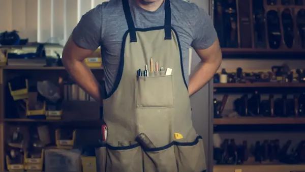 Maker wearing a work apron filled with tools, standing in a tool-lined workshop