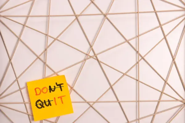 Yellow sticky note reading Dont Quit with Dont crossed to spell Do It on a string grid