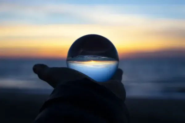 A hand holds a glass sphere inverting a sunset, evoking reflection after a failed startup.