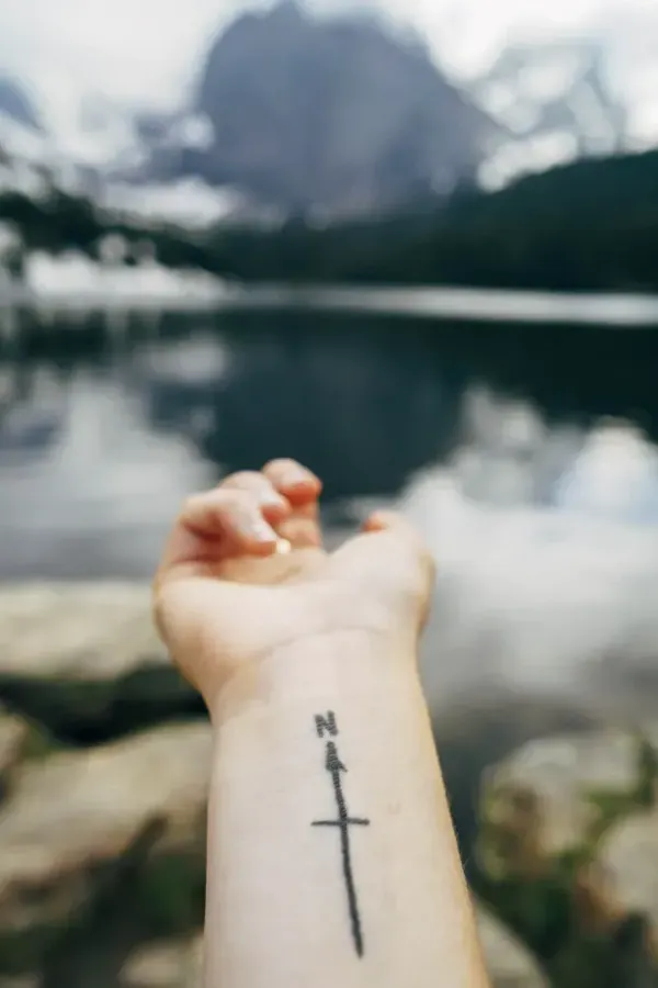 An arm with a compass tattoo reaching toward mountains, symbolizing direction after setbacks.