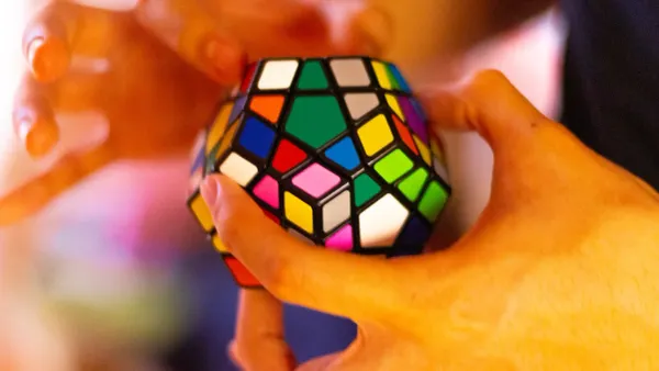Hands twisting a colorful dodecahedron puzzle, a metaphor for untangling complex problems