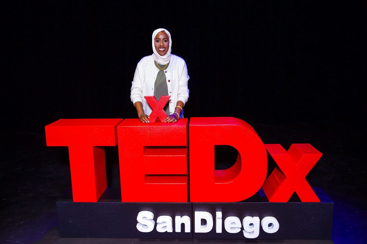 Ramla Sahid standing behind a large sign for TEDx San Diego 