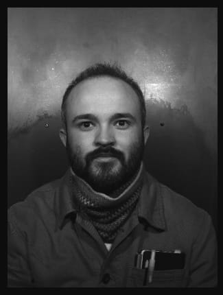 B&W photo of William Davy in a photo booth with a black border. He looks directly into the camera