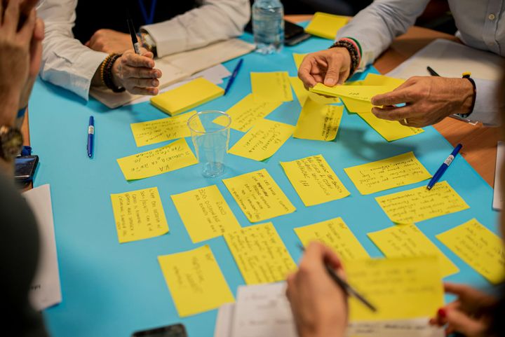People sit around a table, writing and assembling notes in a group brainstorming session.