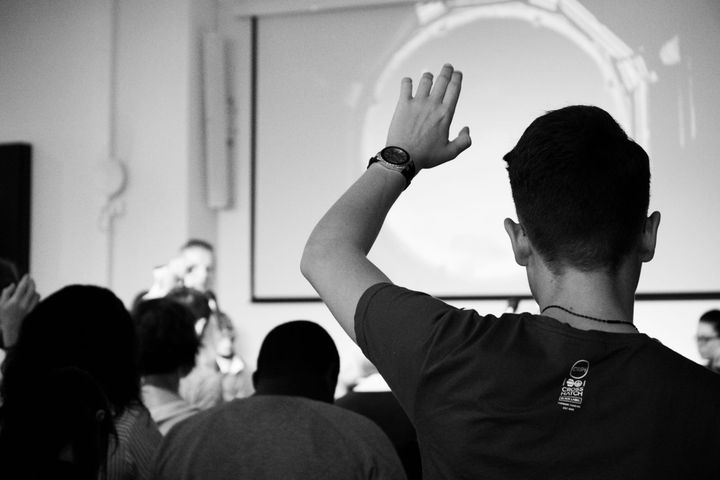 A man raises his hand in a setting that resembles a classroom.