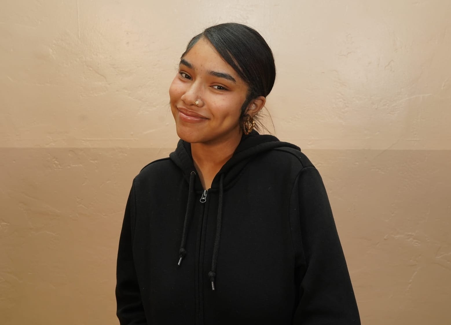 Kennedy Boxie, 20, smiles while wearing a black hooded sweatshirt and gold earrings. She earned California's minimum wage for years while working as a cashier. Now, she's a law clerk earning well above it. Photo courtesy of Los Angeles Black Worker Center.