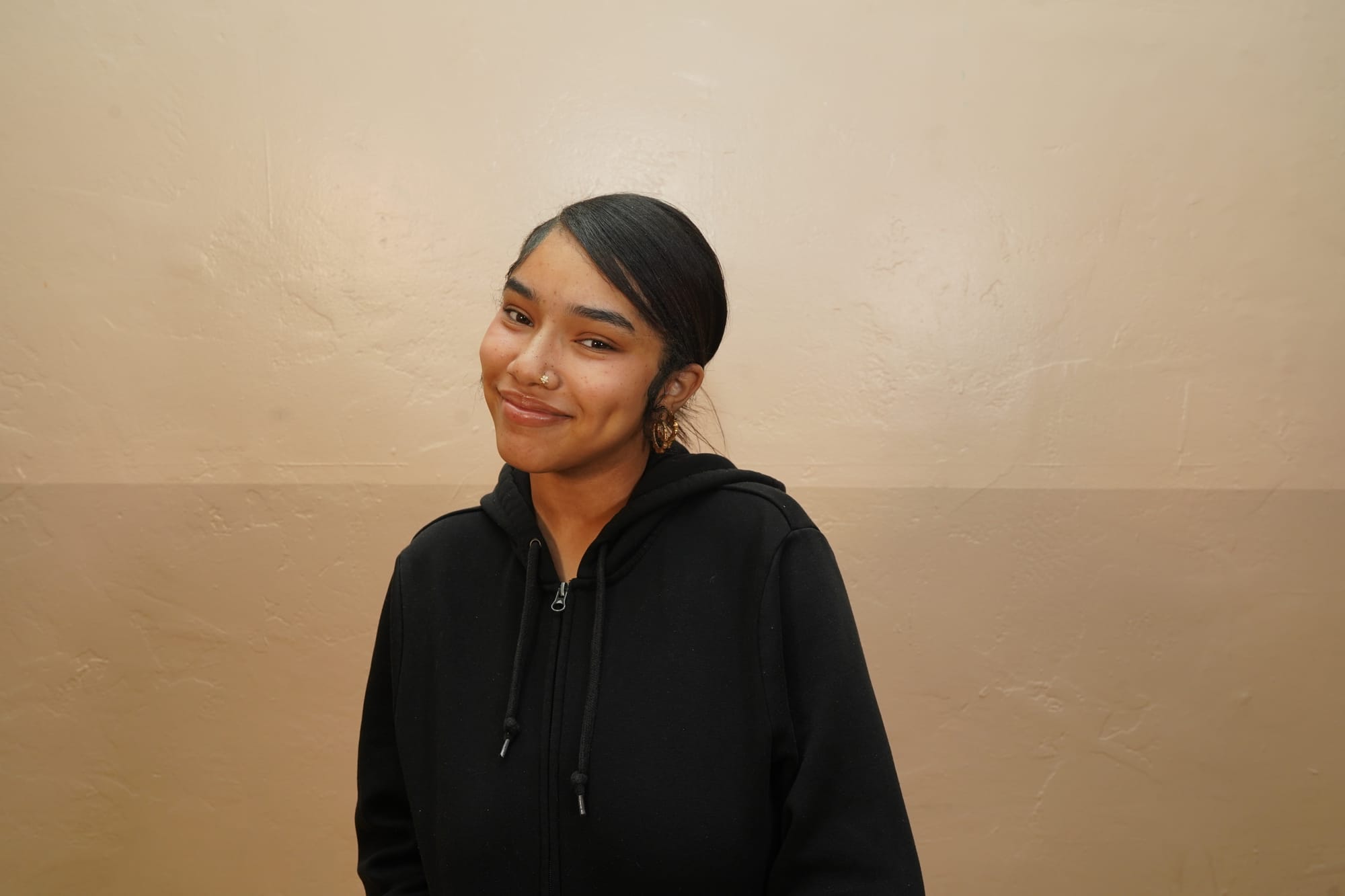 Kennedy Boxie, de 20 años, sonríe mientras viste una sudadera con capucha negra y aretes de oro. Ganó el salario mínimo de California durante años mientras trabajaba como cajera. Ahora, es asistente legal y gana muy por encima de ese salario. Foto cortesía de Los Angeles Black Worker Center.