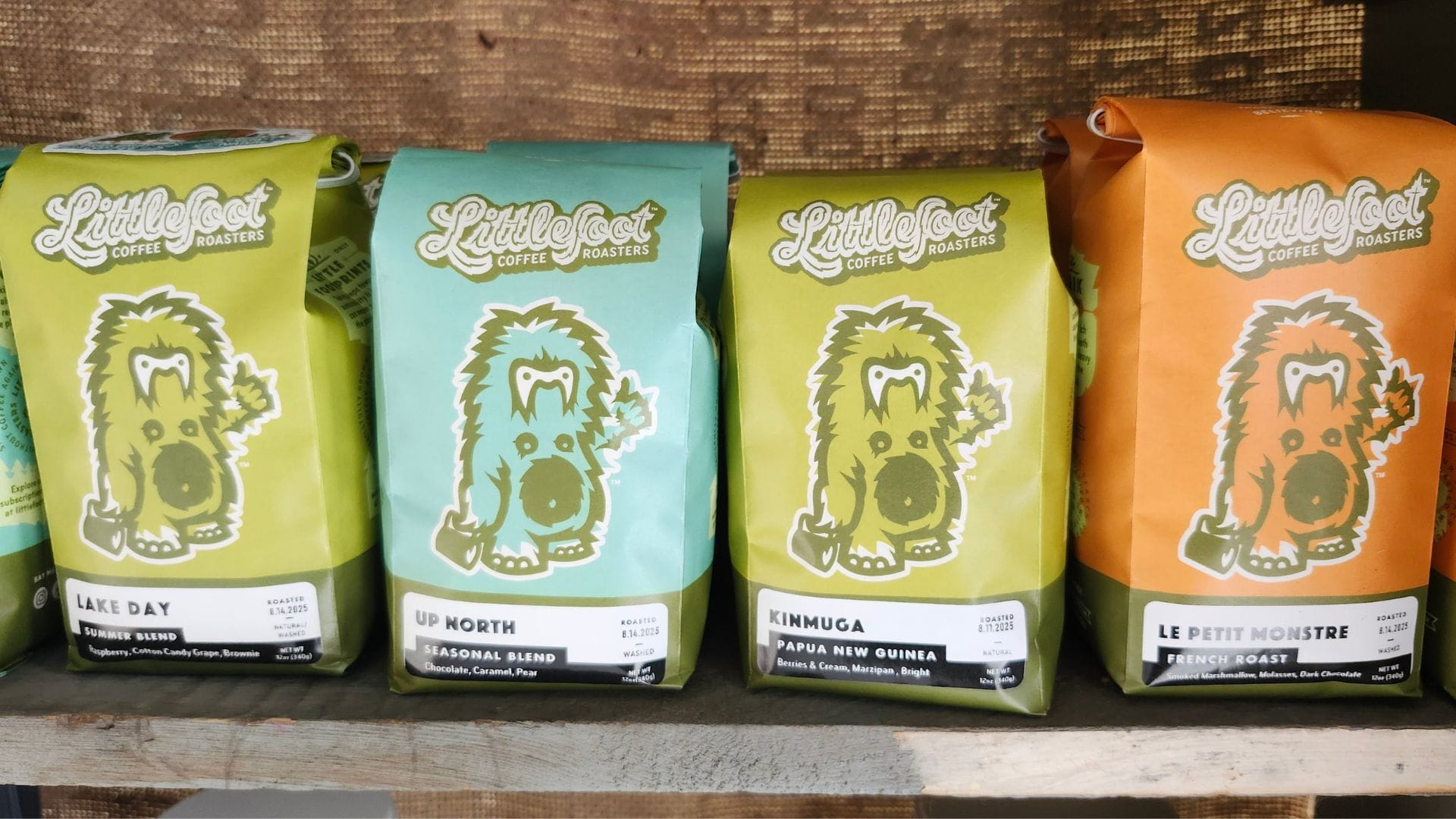 Close-ups of colorful coffee bags with a weird little wookie-like creature on the front sit on a shelf.