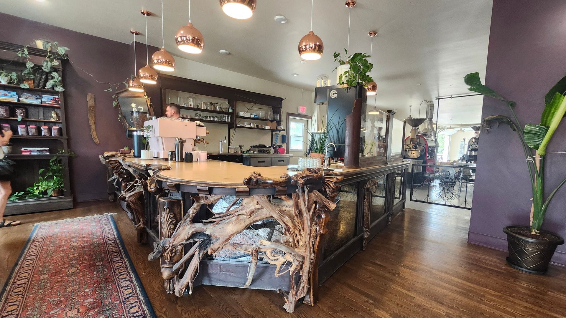 Gnarled wood adorns the front of an L-shaped coffee bar. A pink La Marzocco espresso machine sits on the far left side of the bar.