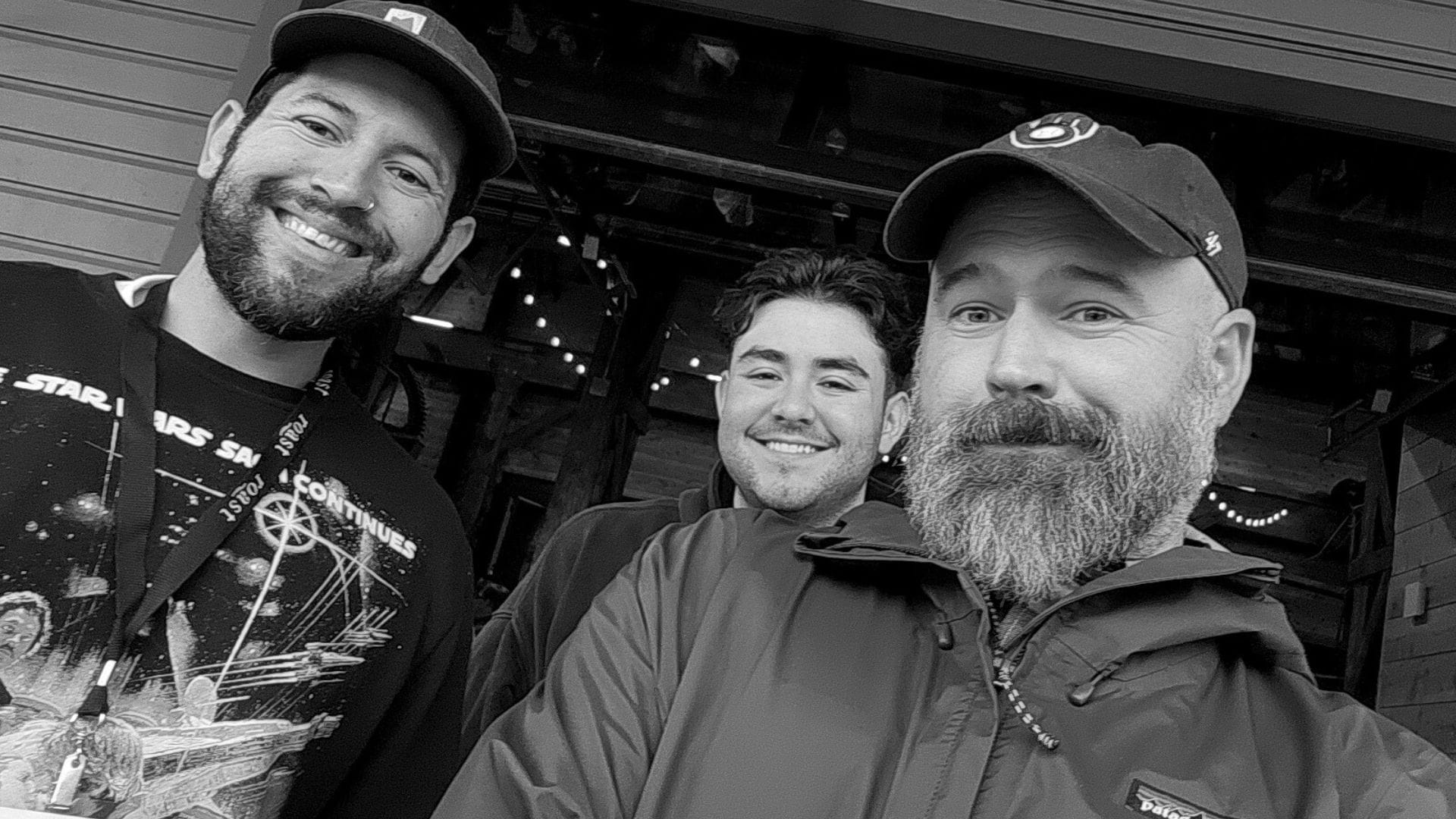 Three guys smile for a camera being held at a low angle.