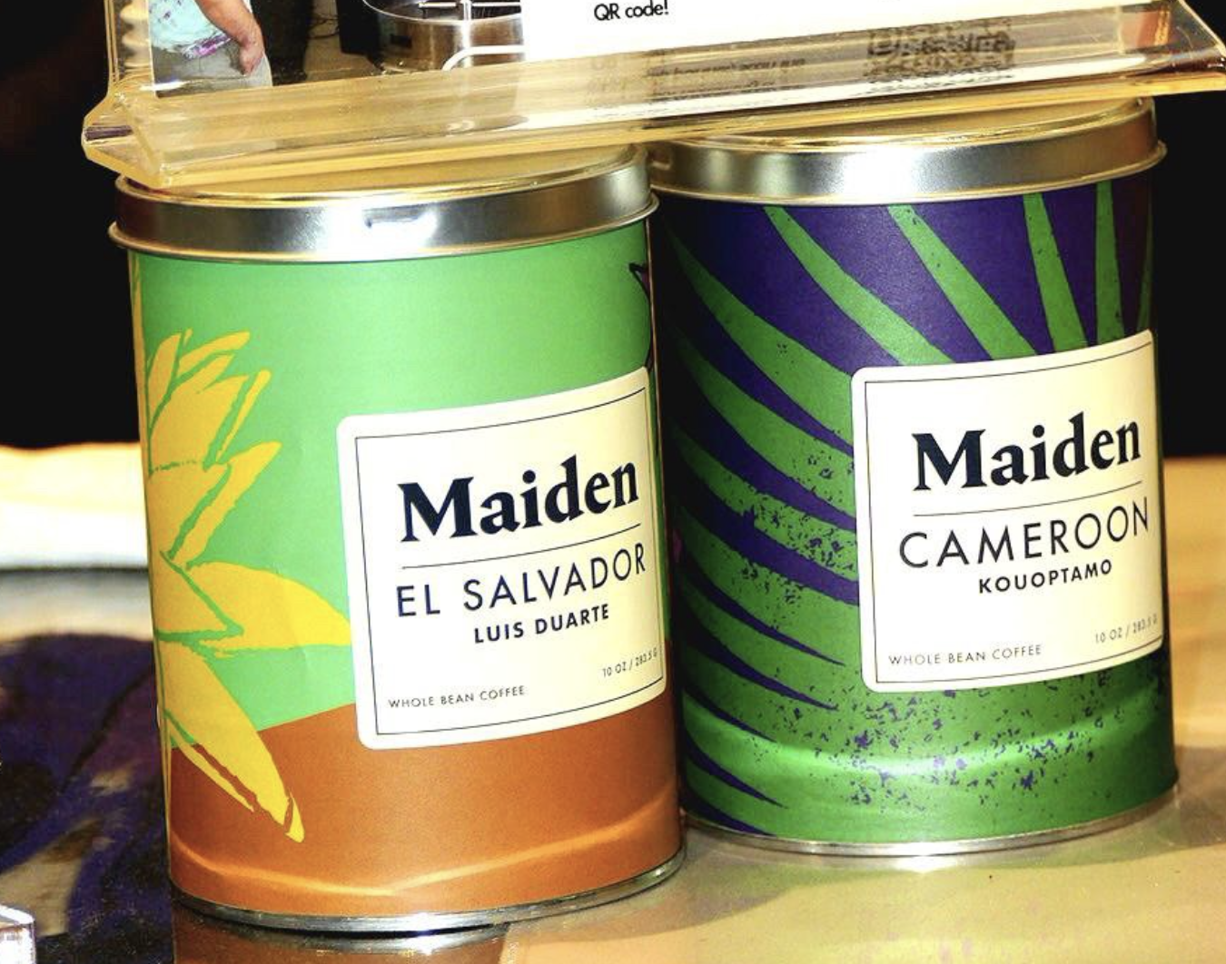 A close up of two brightly labeled coffee cans with white labels indicating the origin. 