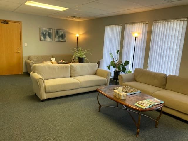 Three comfortable couches and a small coffee table in the confidential waiting room of an East Lansing therapy office