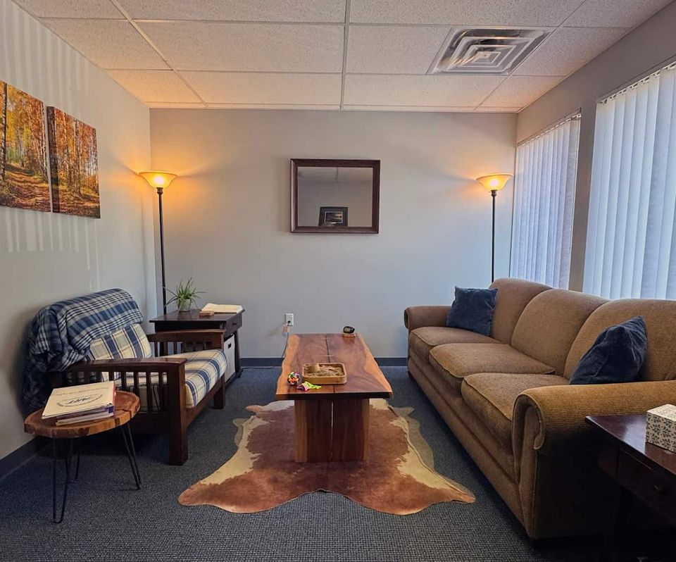 A brightly lit therapy room with a couch, chair, and plants in East Lansing, Michigan