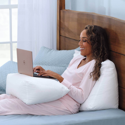 Woman using a laptop while resting on a wedge pillow
