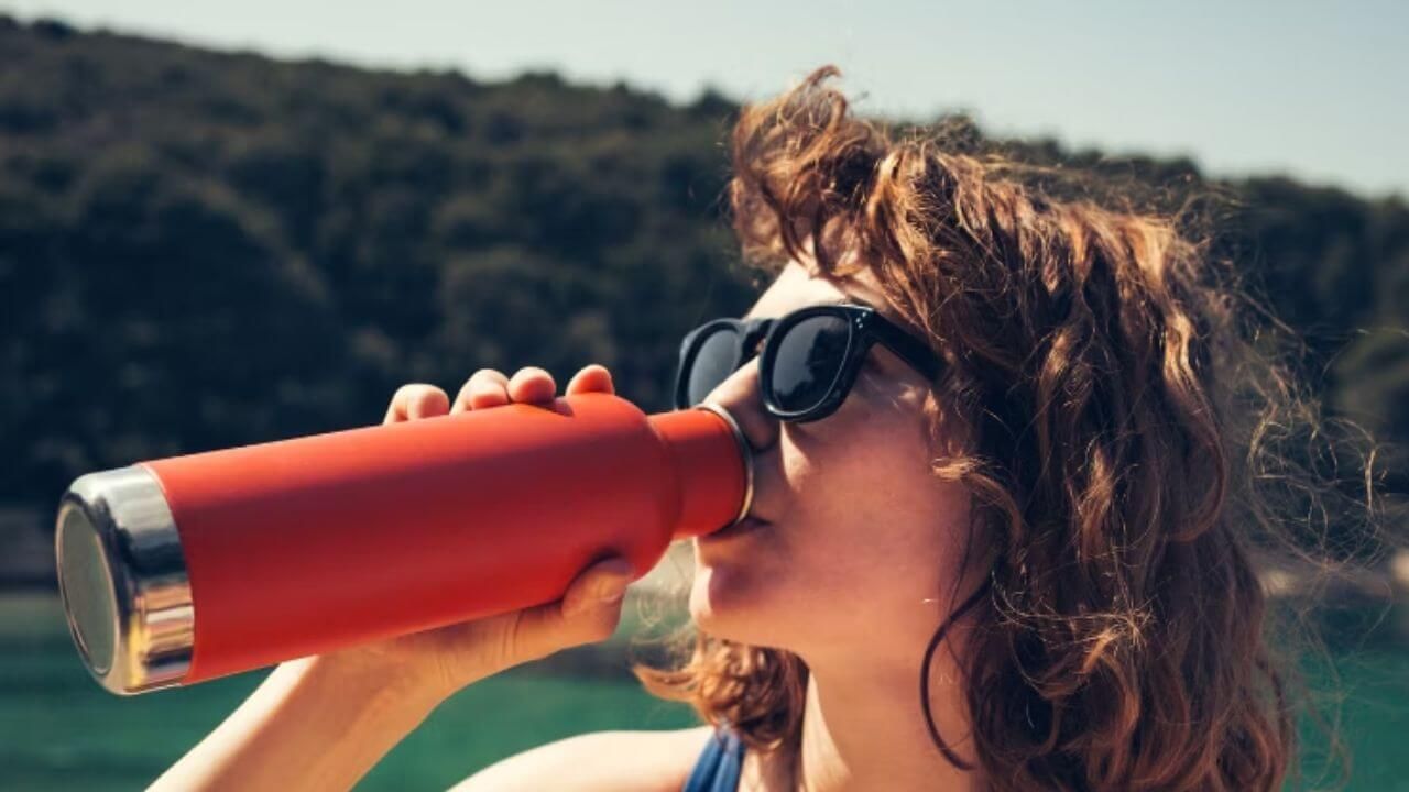 Woman drinking from a red stainless steel water bottle