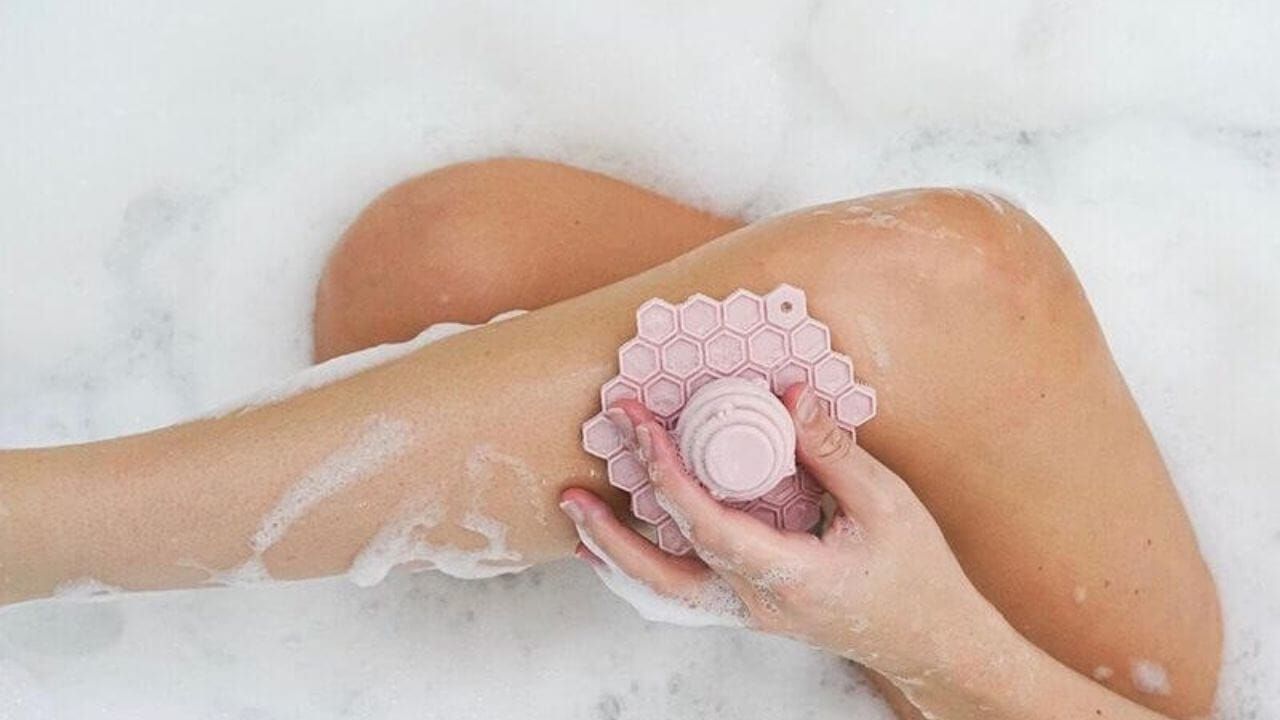 Person using a pink silicone body scrubber while taking a bath