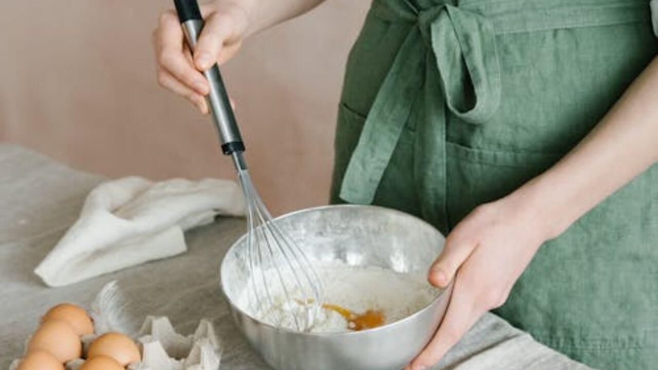 Person mixing baking ingredients in a stainless steel bowl