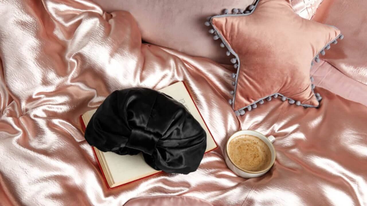 Black silk bonnet resting on a book on a pink satin bedspread next to a cup of coffee