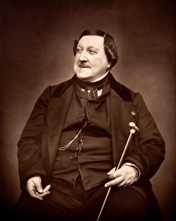 Historische Fotografie: Gioachino Rossini sitzend, in dunklem Gehrock mit Weste, einen Spazierstock in der linken Hand