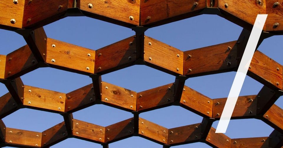 Foto: Eine hölzerne Wabenstruktur aus sechseckigen, verschraubten Holzleisten vor blauem Himmel. Dulcey Lima/Unsplash