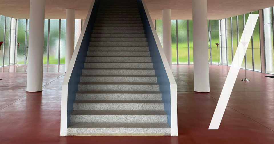 Foto: Eine gerade Treppe steigt mittig durch eine modernistische Halle mit weißen Säulen nach oben. Marek Omasta/Unsplash