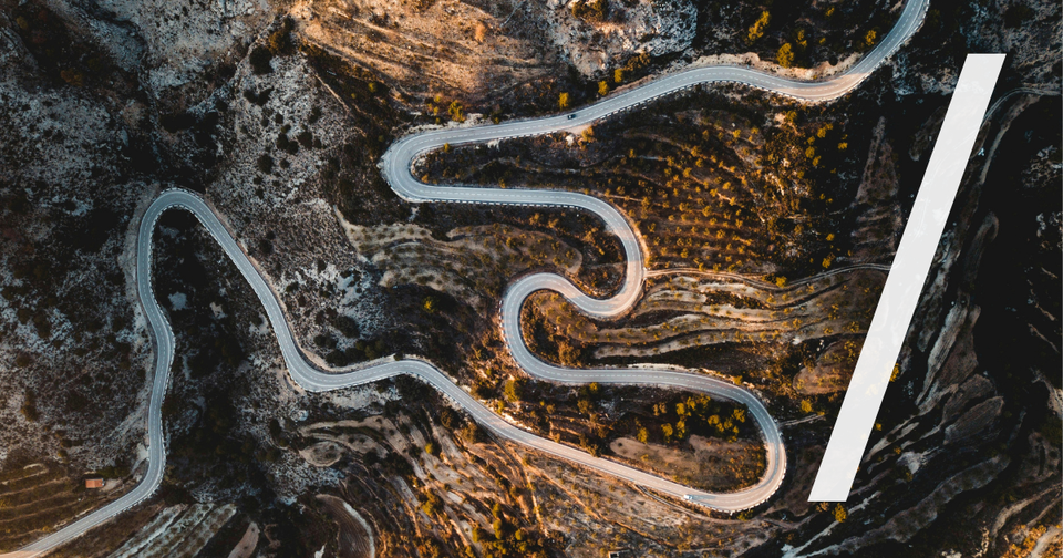 Foto: Luftaufnahme einer kurvigen Straße, die sich durch bergiges Gelände schlängelt. Jack Anstey/Unsplash