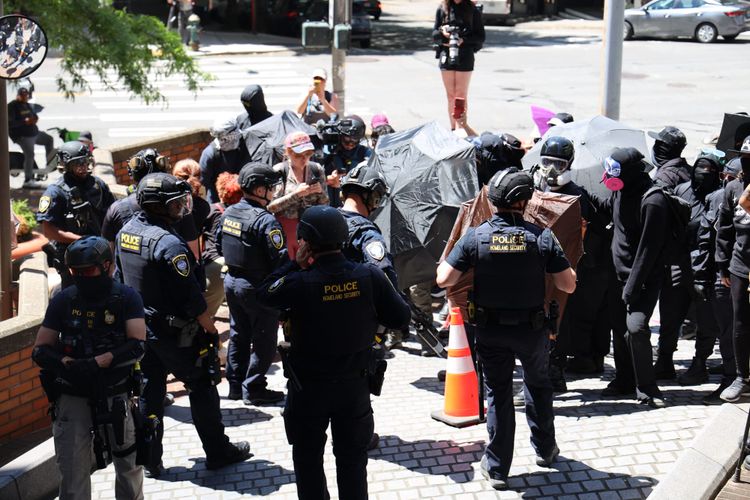 police in riot gear confront protesters holding umbrellas