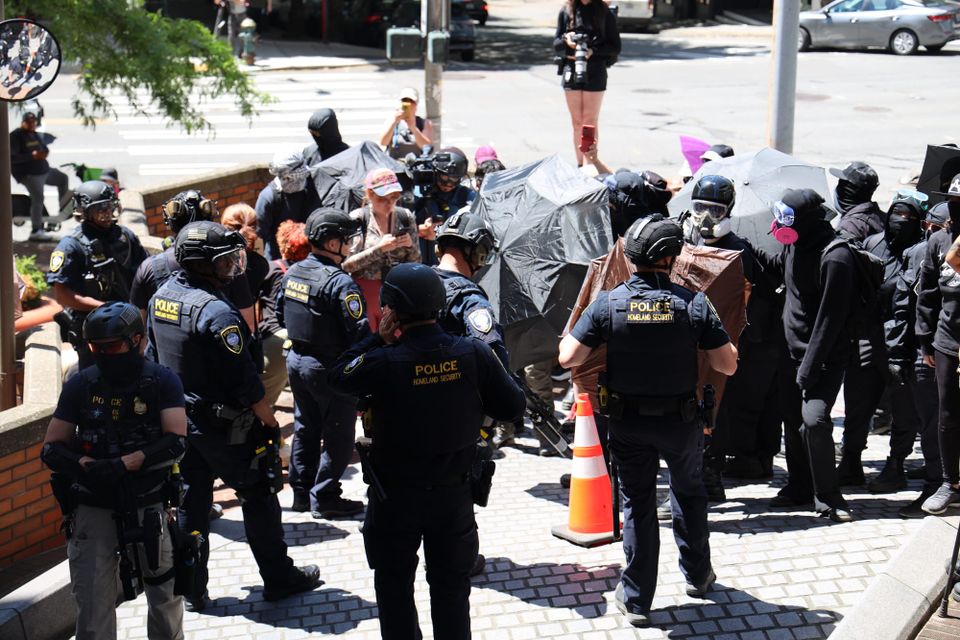 police in riot gear confront protesters holding umbrellas